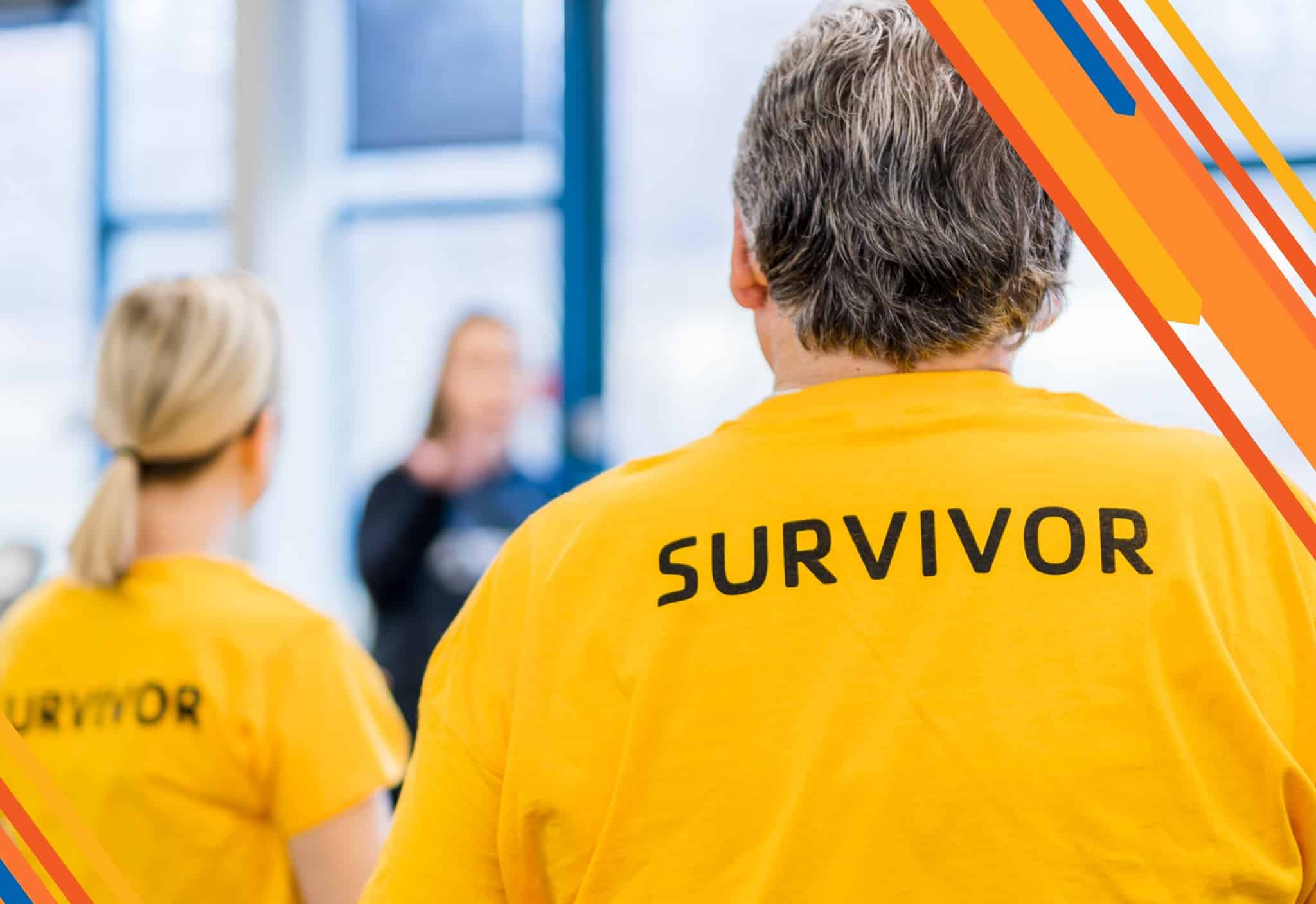 A close-up view from behind of a person wearing a yellow shirt with the word 'SURVIVOR' printed on the back. Another person in a similar shirt is visible in the background, slightly out of focus.